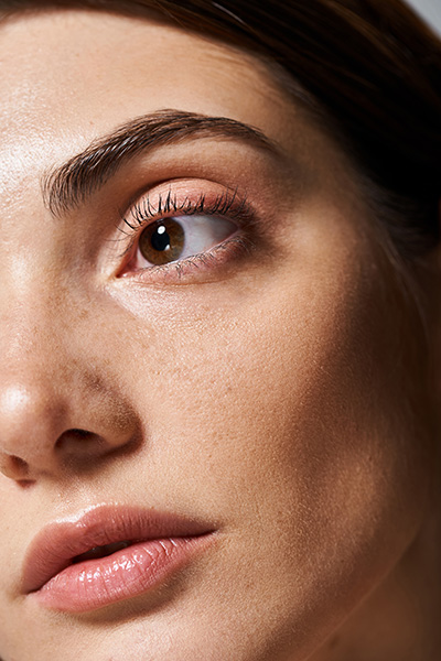 A young caucasian woman with clean skin is featured in a close-up, highlighting her captivating brown eyes